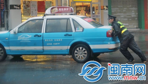 一名協(xié)警奮力推車，幫助的哥將車輛移走
