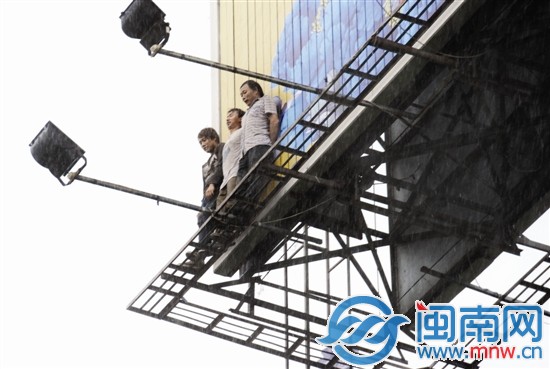 大雨中，幾名工人緊貼廣告牌，但渾身已被淋濕